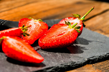 Juicy red freshly cut in half strawberries on a stone texture background. Close up sunlit half of strawberries.