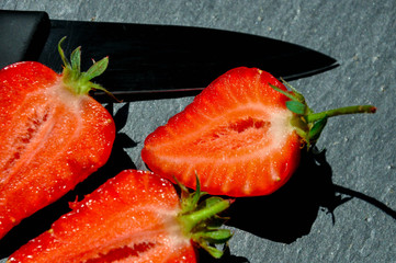 Juicy red freshly cut in half strawberries on a stone texture background. Close up sunlit half of strawberries.