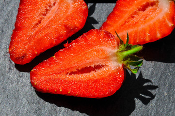 Juicy red freshly cut in half strawberries on a stone texture background. Close up sunlit half of strawberries.