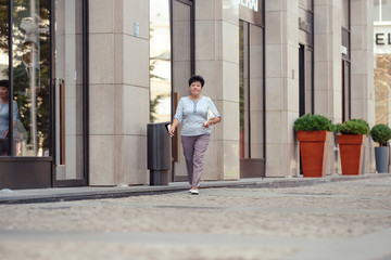 Aged woman wearing casual clothes while walking on the street.