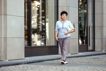 Aged woman wearing casual clothes while walking on the street.