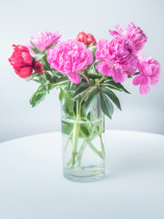 glass vase on the white table with pink peons in close up view