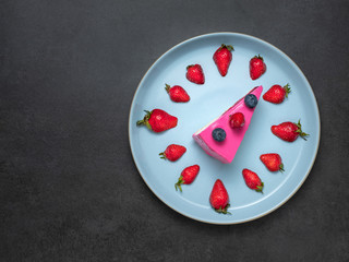 overhead view to pink strawberries cake on blue plate with strawberries like a clock on dark background with copy space