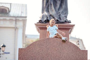Obraz premium Portrait of a lovely little girl siiting and having fun on the monument in park.