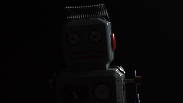 Dramatic Closeup of light illuminating a retro vintage small robot standing in the dark,  while it passes over it