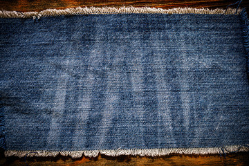 Denim blue cloth frame patch on wooden table. Denim jeans frame background. Ripped denim fabric,...
