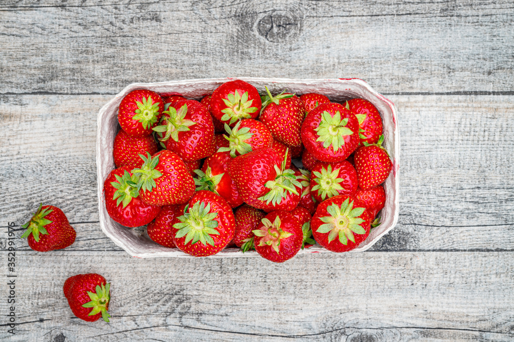 Wall mural Fresh German strawberries in carton paper boxes on wooden table, top view.  Red strawberry berrees harvesting concept