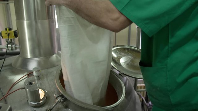 A Brewer In Green Work Clothes Adds Ingredients To A Tank Where Beer Ferments Mixing