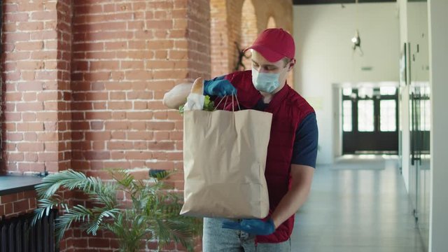 Volunteer man in protective mask and gloves pack products. Food delivery courier services during coronavirus pandemic for working from home and social distancing. Shopping online.