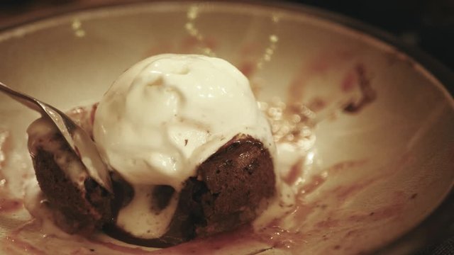 Dessert fondant, ice cream ball on hot chocolate cake on plate, breaks a chocolate cake, liquid chocolate flows, toned, close up