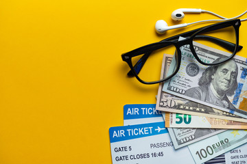 Travel concept - glasses, money, airline tickets and headphones on a yellow background with copy space