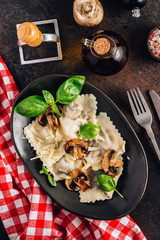 Italian cuisine - ravioli pasta with champignon mushrooms and parmesan cheese on black plate on dark background.