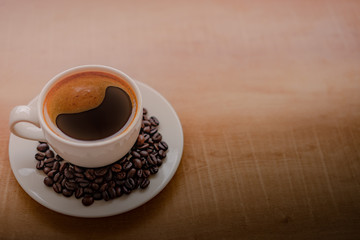 Rich coffee with a soft creamy foam in a white coffee cup with coffee beans on the plate. Try the glass on a wooden table with space to put text.