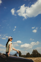 Obraz premium Outdoor adventure. Young woman sitting on the car hood while traveling. Tourism lifestyle, vacation, freedom and travel concept