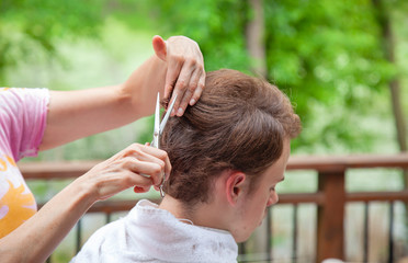 Obraz premium Young man gets a haircut outdoors from his mother during the pandemic