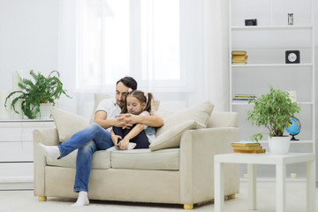 Father and his daughter having fun, sitting on sofa together.