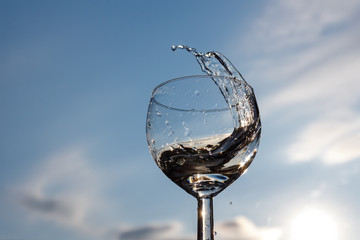 Splash of water in a wine glass against the sky in backlit sunlight.