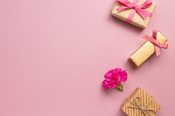 Gift boxes with carnation flower on pink background. Anniversary concept, flat lay, top view, copy space