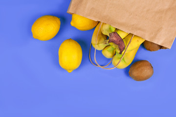 Bananas, kiwi and lemons in a paper eco friendly bag on a purple background. Eco shopping concept.