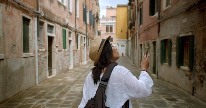 Female traveller looking up at street signs and map trying to find her way wearing fedora and using her mobile phone to find her way in Venice Italy