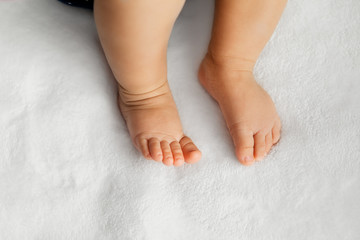 Baby legs on soft white blanket as a background at natural light, infant feet in a selective focus