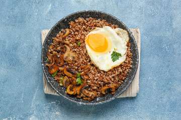Bowl of tasty buckwheat porridge, egg and mushrooms on color background