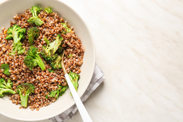 Bowl of tasty buckwheat porridge and broccoli on table