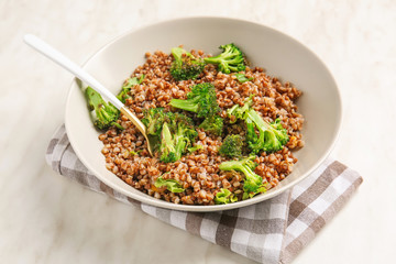 Bowl of tasty buckwheat porridge and broccoli on table