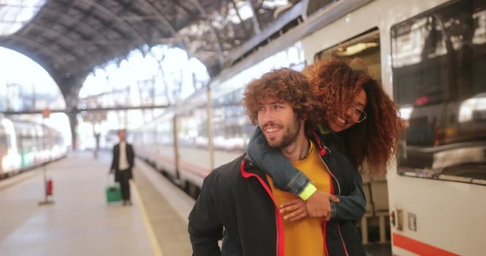 Multi-ethnic couple leaving train girlfriend piggybacking boyfriend at train station
