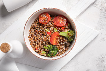 Bowl of tasty buckwheat porridge and vegetables on table