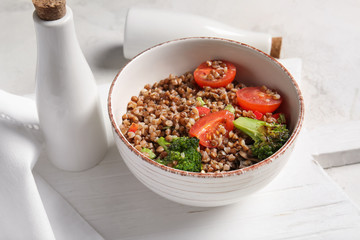 Bowl of tasty buckwheat porridge and vegetables on table