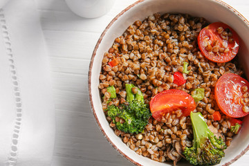 Bowl of tasty buckwheat porridge and vegetables on table