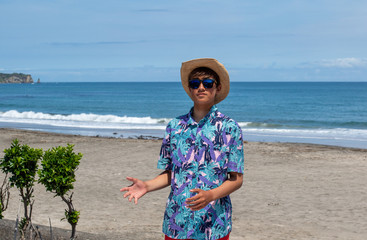 Catching a ball on the beach, an Asian Japanese teenage boy wearing a Hawaiian Shirt catching a ball on the beach in Japan the ocean is blue & he has a suntan.