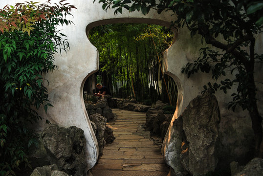 A view of Chinese styled gate in a shape of vase in the Chinese garden with bamboo trees and stones in Beijing, China. A tourist reading a guide in the background.