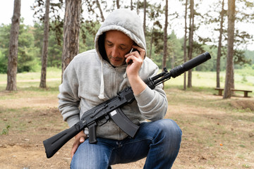 Caucasian adult man in the woods nature in day making a phone call talking while holding the rifle...