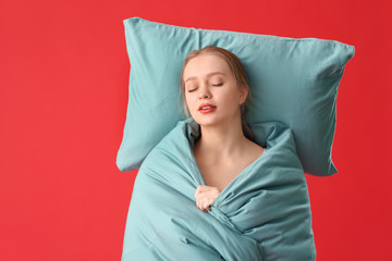 Fototapeta premium Sleepy young woman with pillow and blanket on color background
