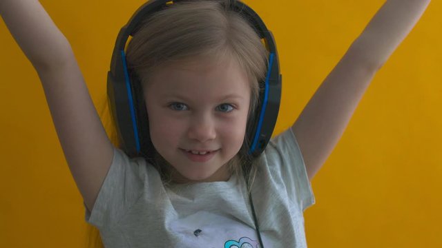 little blonde with blue eyes in headphones plays a video game with a gamepad on a yellow background.