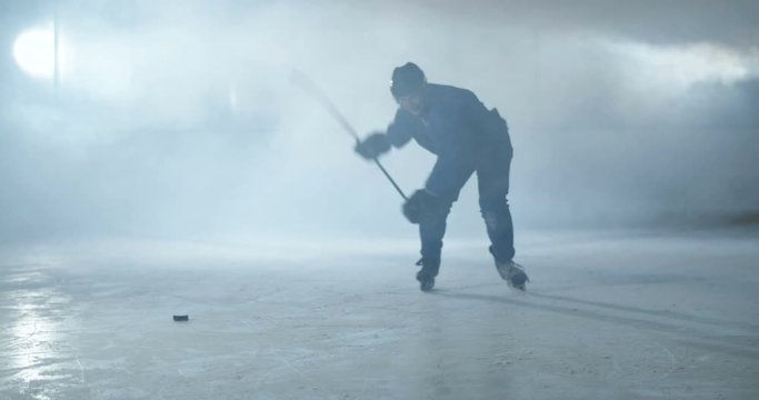 Caucasian male hockey player in uniform, skaters and helmet sliding fast on icy arena and hitting puch with stick during game. Sportsman with club skating and hits disc on ice.