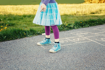 Closeup of child girl playing jumping hopscotch outdoors. Funny activity game for kids on playground outside. Summer backyard street sport for children. Happy childhood lifestyle.