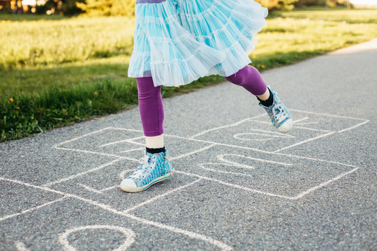 Closeup of child girl playing jumping hopscotch outdoors. Funny activity game for kids on playground outside. Summer backyard street sport for children. Happy childhood lifestyle.
