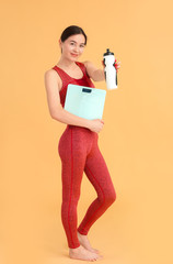 Young woman with weight scales and bottle of water on color background