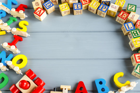 Close up Multicolored wooden cubes with letters, pencils, rainbow arc on gray background. Set of toys for studying alphabet. Education, back to school concept. Top view, copy space - Powered by Adobe