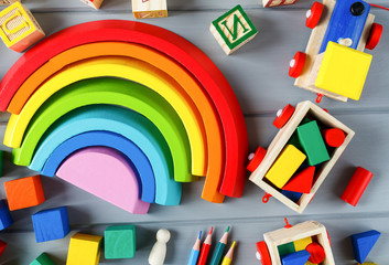 Close up Multicolored wooden cubes with letters, pencils, rainbow arc on gray background. Set of toys for studying alphabet. Education, back to school concept. Top view, copy space
