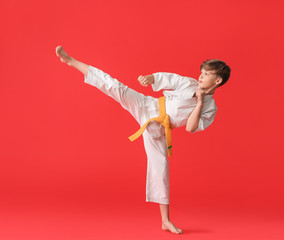 Cute little boy practicing karate on color background