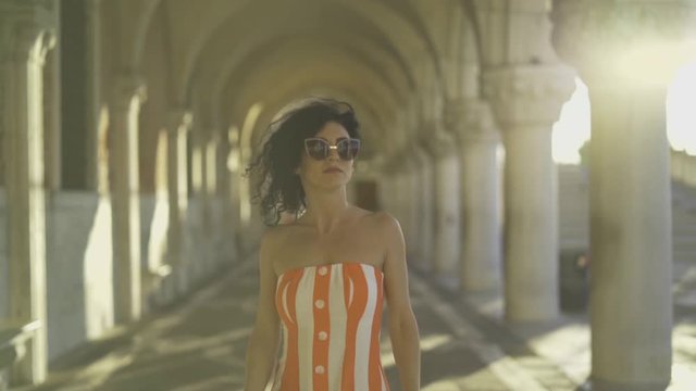 Beautiful woman walking under palace arches at sunrise in slow motion