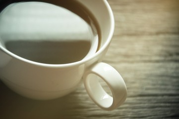 A coffee cup on the wooden textured, Blurred, white coffee mug with Reflection from sun light in a cup black coffee