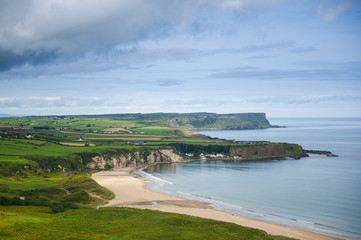 Fototapeta na wymiar Costal view near Ballitoy, County Atrim, Northern Ireland. Beautiful green landscape with cliffs and sandy beaches. Some buildings are visible.