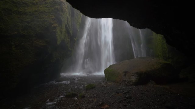 Deep in a rocky gorge in Iceland, Gljufrabui waterfall spills down the cliff and runs out of the cave through a stream
