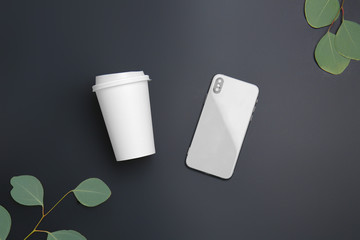 Takeaway cup for drink and mobile phone on dark background