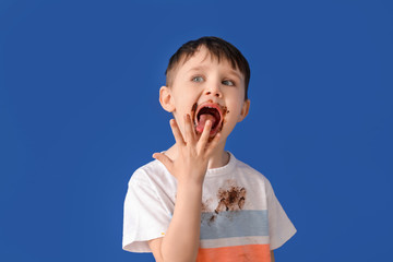 Little boy in dirty clothes eating of chocolate on color background